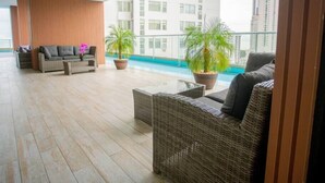 A spacious balcony with wicker furniture, a pool, and a city view.