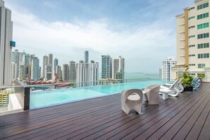 Un área de piscina en la azotea con vista a la ciudad, sillones de descanso y una terraza de madera.