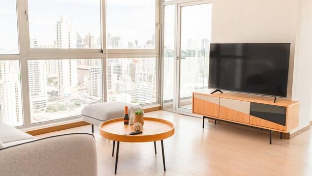 Ein modernes Wohnzimmer mit einem großen Fernseher, einem runden Holztisch und einer Couch.