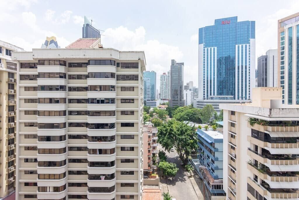 A high-rise building with multiple balconies, surrounded by other tall buildings and trees.