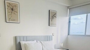 A modern hotel room with a large bed, a bedside table, a nightstand, and two framed botanical prints on the wall.
