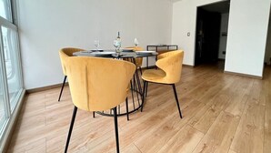 A dining area with a round table and four yellow chairs, a window with a view, and a wooden floor.