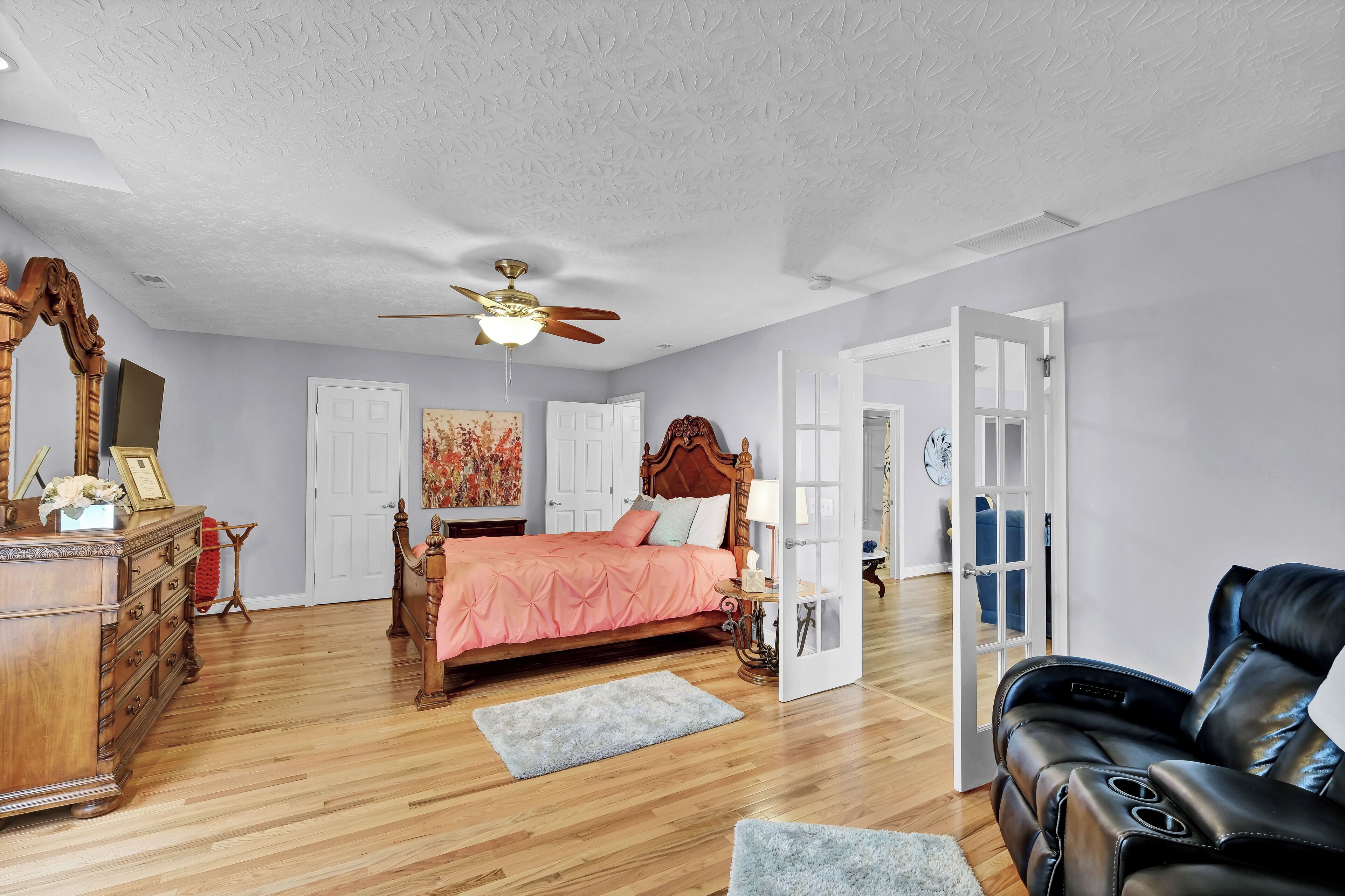 Une chambre à coucher avec un lit en bois, un ventilateur de plafond, une commode et un fauteuil de massage.