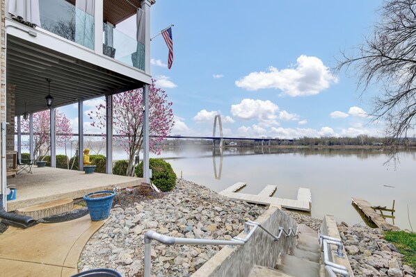 Une propriété au bord du lac, dotée d’un patio couvert, d’un quai et offrant une vue sur un pont situé au loin.
