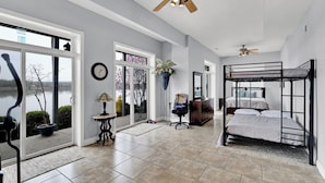 A spacious room with a large window, a ceiling fan, a bunk bed, and a potted plant. - Beautiful views and sunrises overlooking the water. Spacious home with elevator. (Jeffersonville)