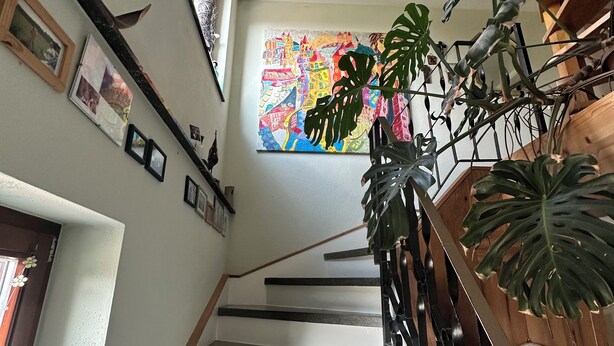A staircase with a wooden railing, a colorful abstract painting on the wall, and a large plant.