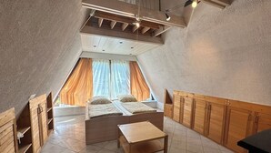 A loft-style bedroom with a sloped ceiling, a bed with two pillows, a wooden table, and built-in wooden cabinets.