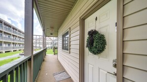 Een overdekte veranda met een deur, een groene balustrade en uitzicht op een gebouw met meerdere ramen en balkons.
