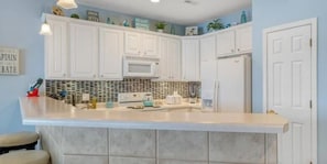 A kitchen with white cabinets, a microwave, a refrigerator, and a tiled backsplash. - Next door to Dog Days Grill! Waterfront with amazing views! JACUZZI TUB (Osage Beach)