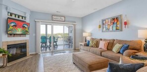 A living room with a fireplace, a sofa, a coffee table, and a TV. There is a sliding glass door leading to a balcony with outdoor furniture. - Next door to Dog Days Grill! Waterfront with amazing views! JACUZZI TUB (Osage Beach)