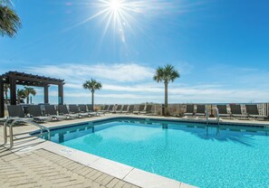 A clear blue swimming pool with lounge chairs and a pergola, surrounded by palm trees. - ☀️Gulf Front-Large Balcony-Pool +  Hot Tub-2BR Ocean Villa 2004☀️ (Panama City Beach)