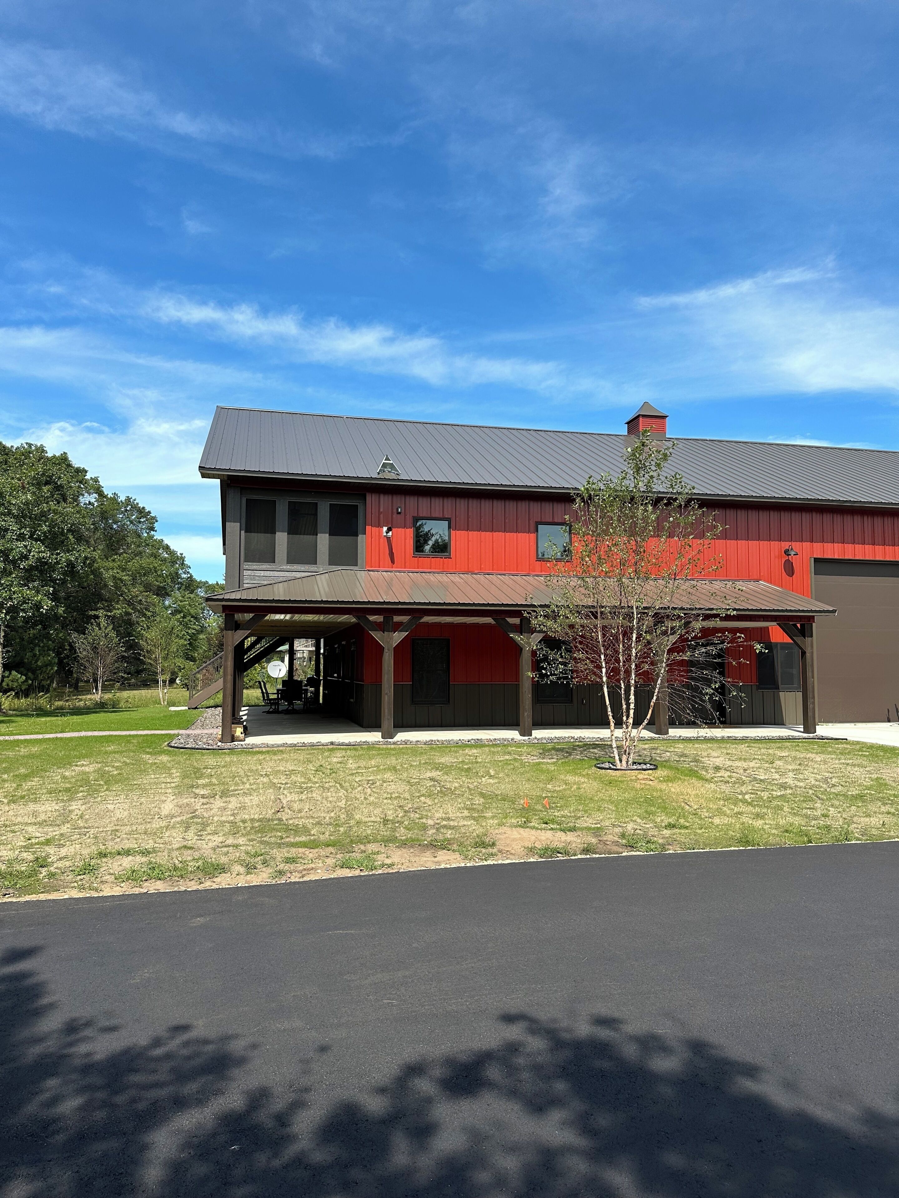Un edificio de dos pisos con fachada roja y gris, un patio cubierto y un pequeño árbol en la parte delantera.