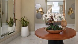 A modern lobby with a round wooden table, potted plants, and decorative wall art. - Sunrise Suites (Puerto Plata)