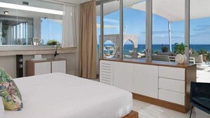 A hotel room with a large bed, a desk, a chair, and a view of the ocean. - Sunrise Suites (Puerto Plata)