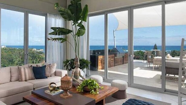A spacious living room with a large sofa, a coffee table, and a view of the ocean through large windows. - Sunrise Suites (Puerto Plata)