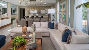 A modern living room with a sofa, coffee table, and a TV. There is a dining area in the background. - Sunrise Suites (Puerto Plata)