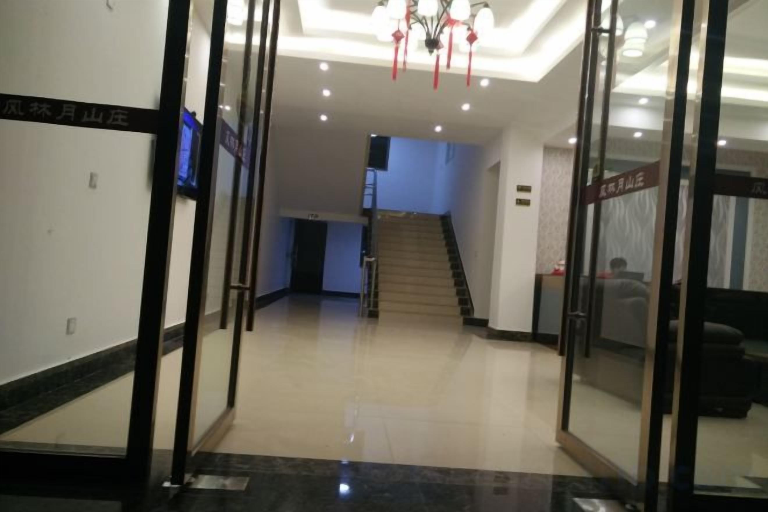 A hotel lobby with a staircase, a reception desk, and a glass door entrance.