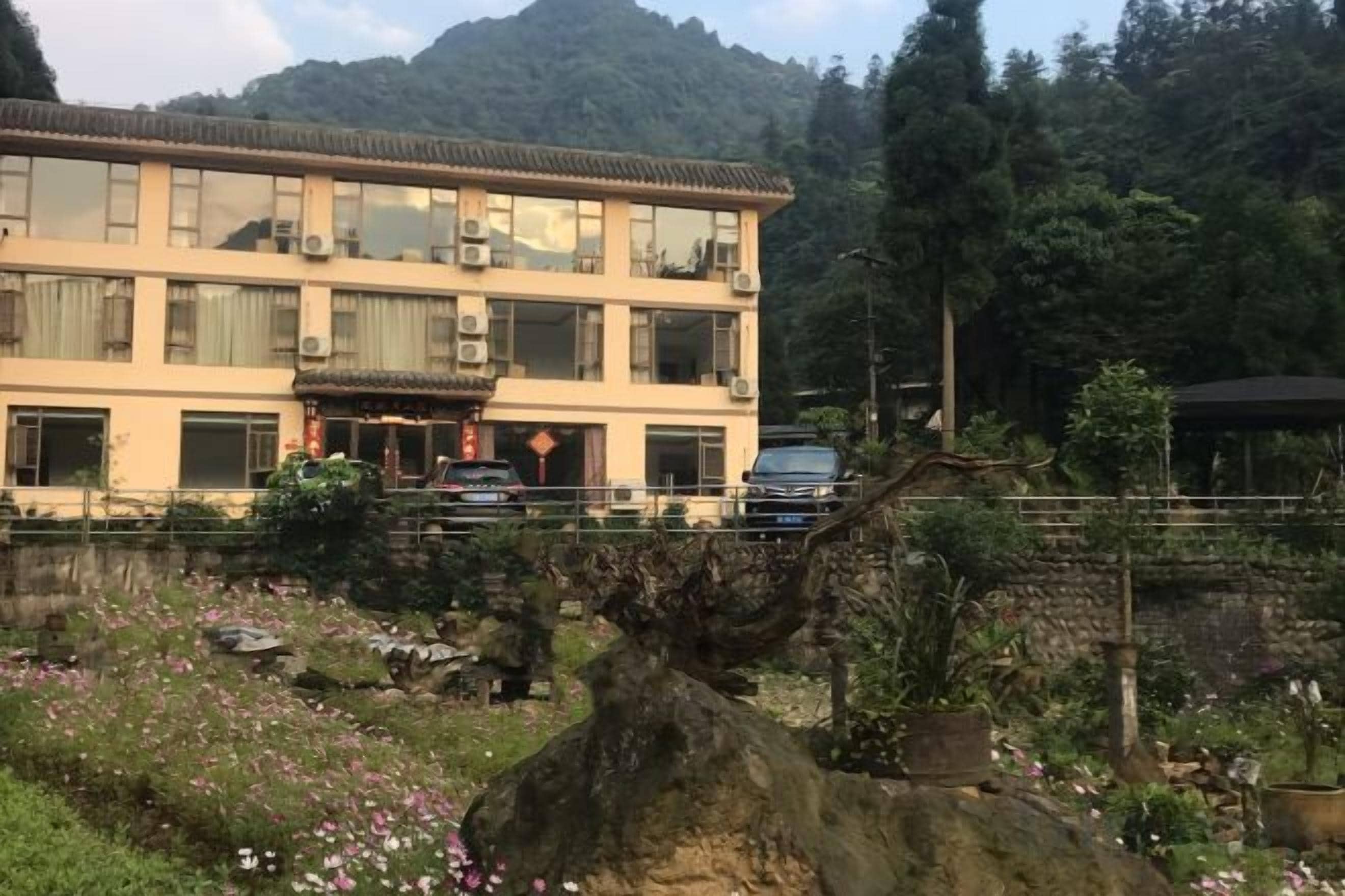 Un edificio de varios pisos con estilo arquitectónico tradicional, rodeado de un jardín ajardinado con plantas en flor y una gran roca ornamental.