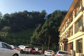 Un aparcamiento con varios coches, un edificio con amplias ventanas y una colina arbolada al fondo.