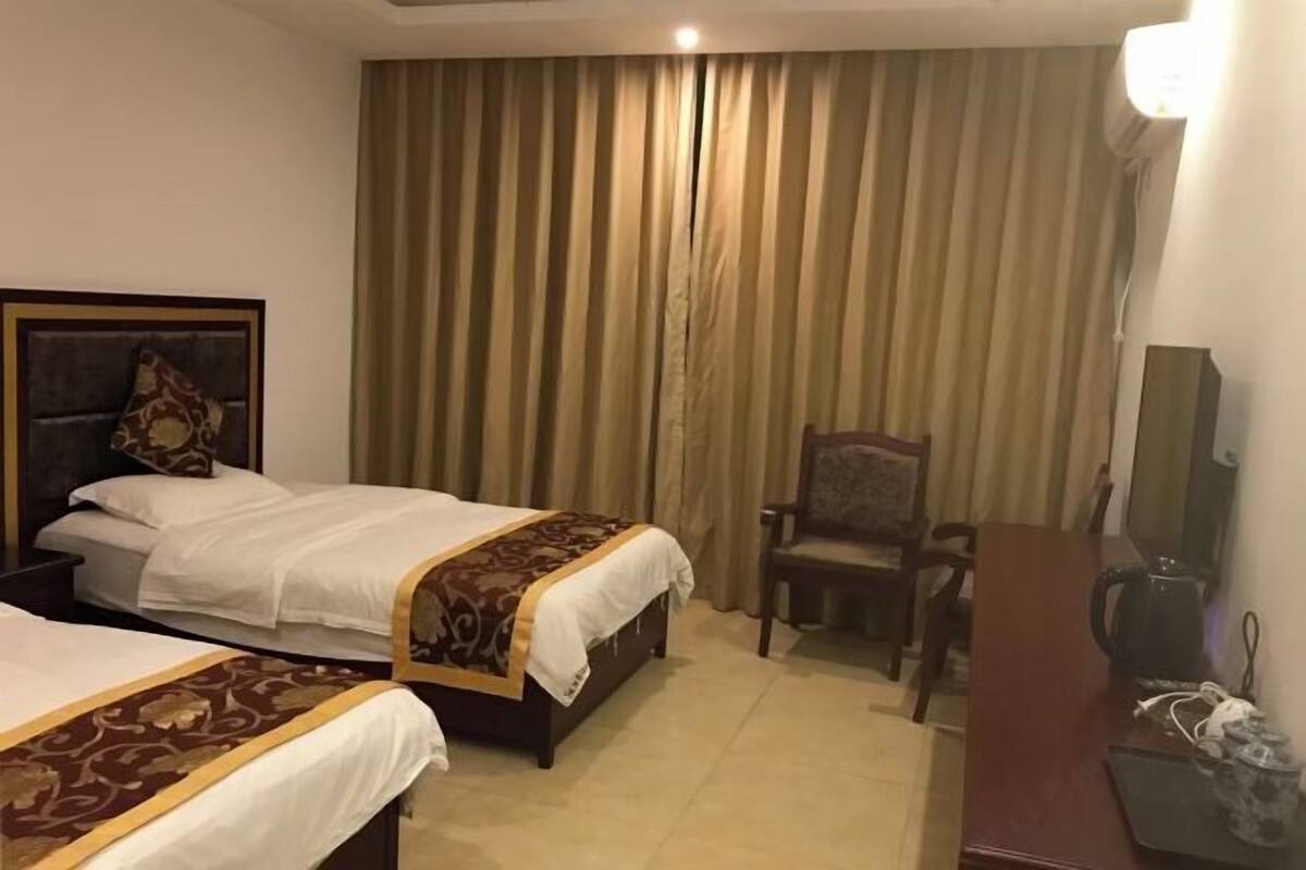 A hotel room with two beds, a desk, a chair, and a television.