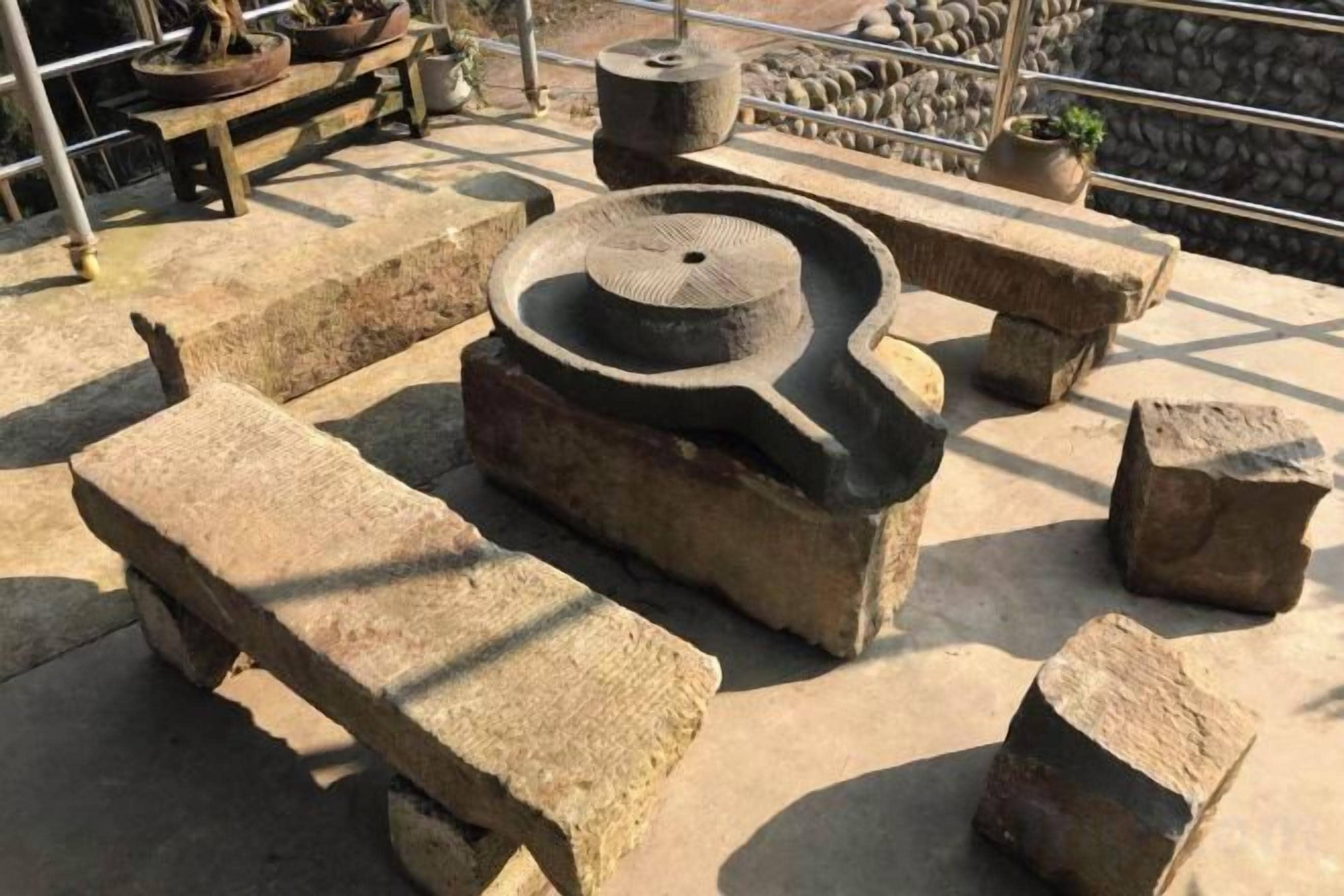 Una estructura de piedra con una cuenca circular, posiblemente una fuente, rodeada de bancos de piedra.