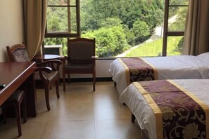 A hotel room with a bed, a desk, and a chair. There is a window with a view of greenery outside. - Mount Emei Feng Lin Yue Hotel (Emeishan City)