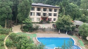 A multi-story building with a pool, surrounded by dense forest.