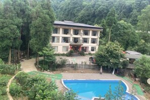 A multi-story building with a swimming pool surrounded by greenery. - Mount Emei Feng Lin Yue Hotel (Emeishan City)