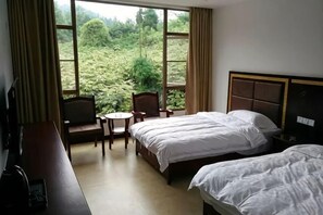 A hotel room with two beds, a desk, a chair, and a window with a view of greenery. - Mount Emei Feng Lin Yue Hotel (Emeishan City)