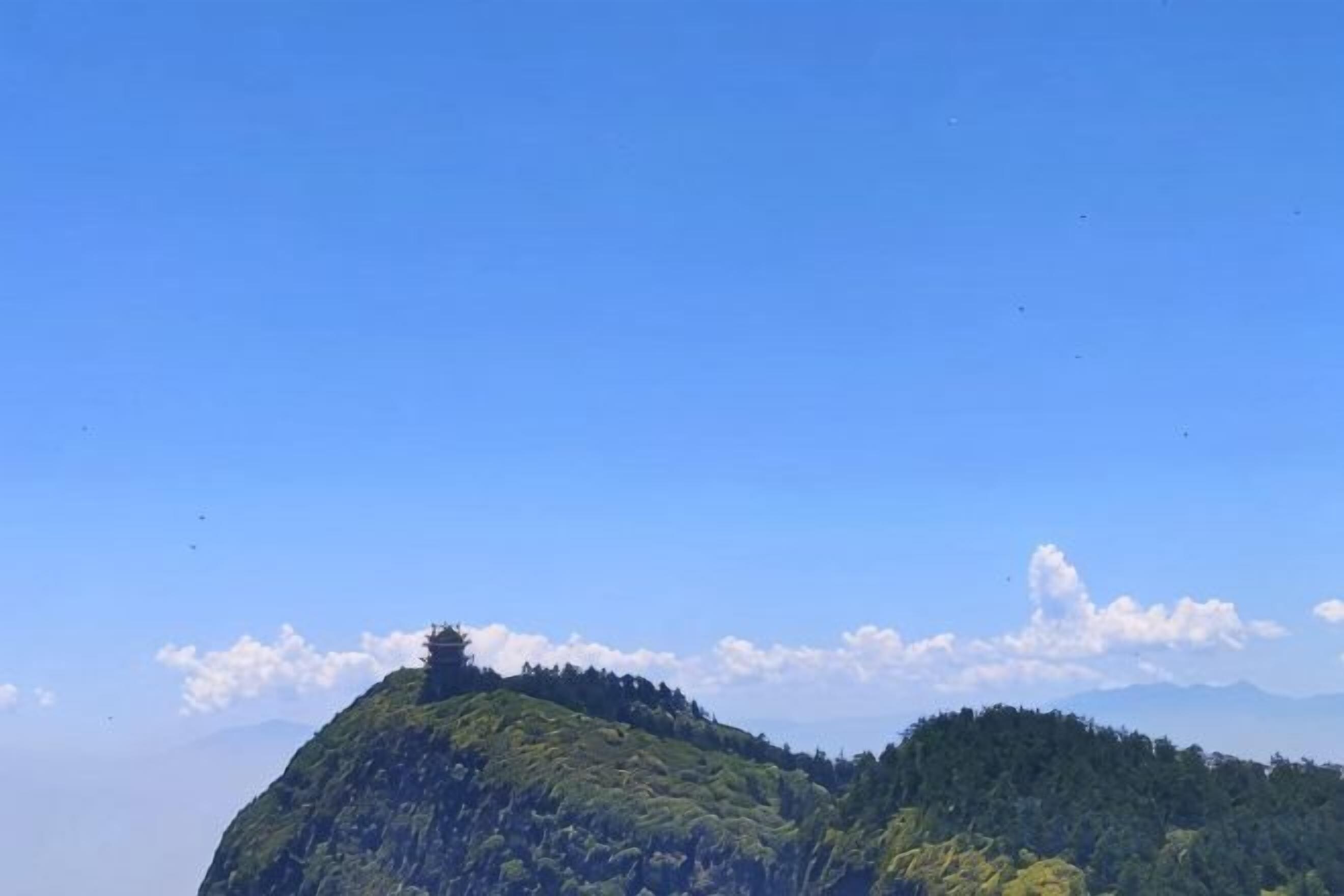A clear sky above a green hill with a small structure on top.