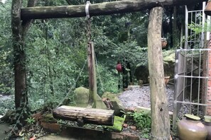 A rustic wooden swing suspended by a rope, surrounded by lush greenery and a small brick structure. - Mount Emei Feng Lin Yue Hotel (Emeishan City)