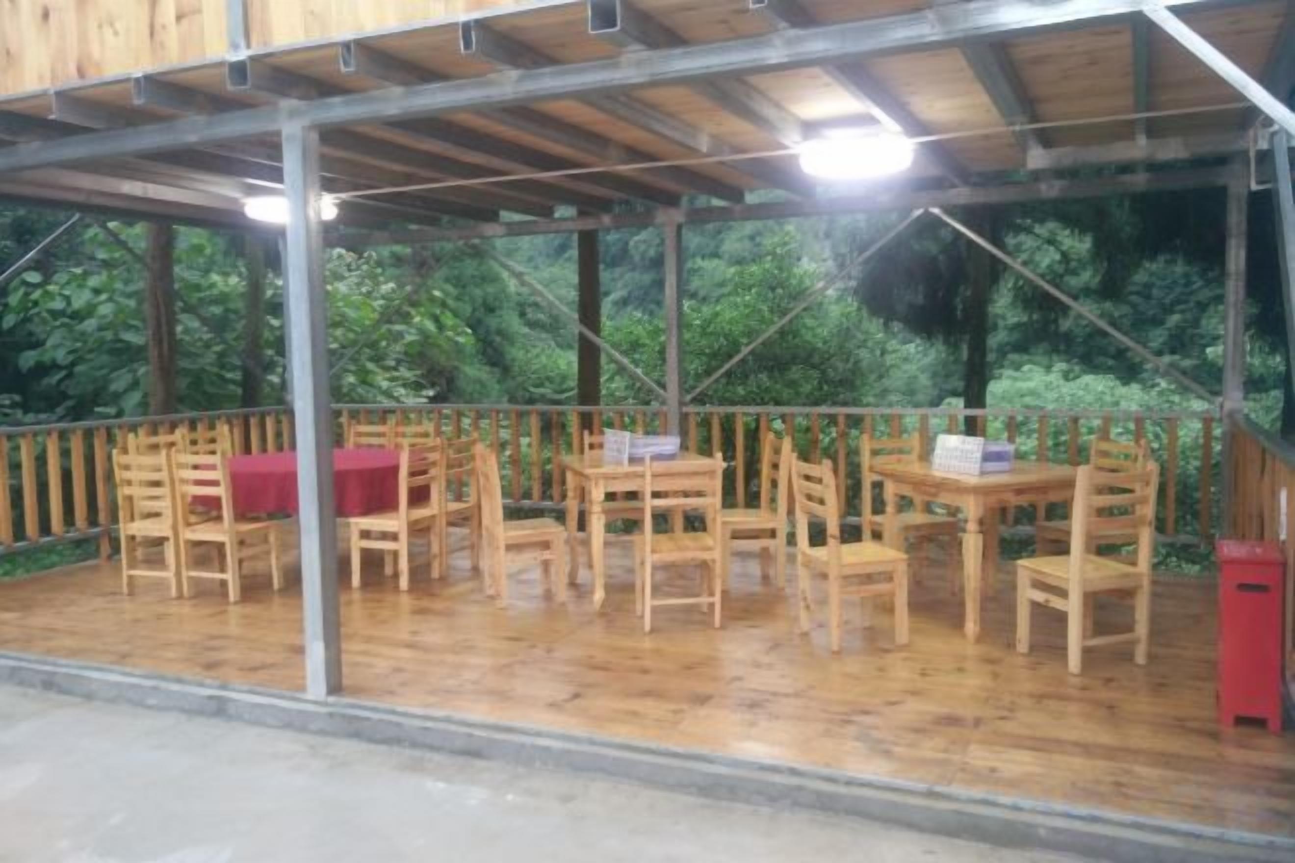Un patio techado al aire libre con mesas y sillas de madera, rodeado por un cerco de madera.
