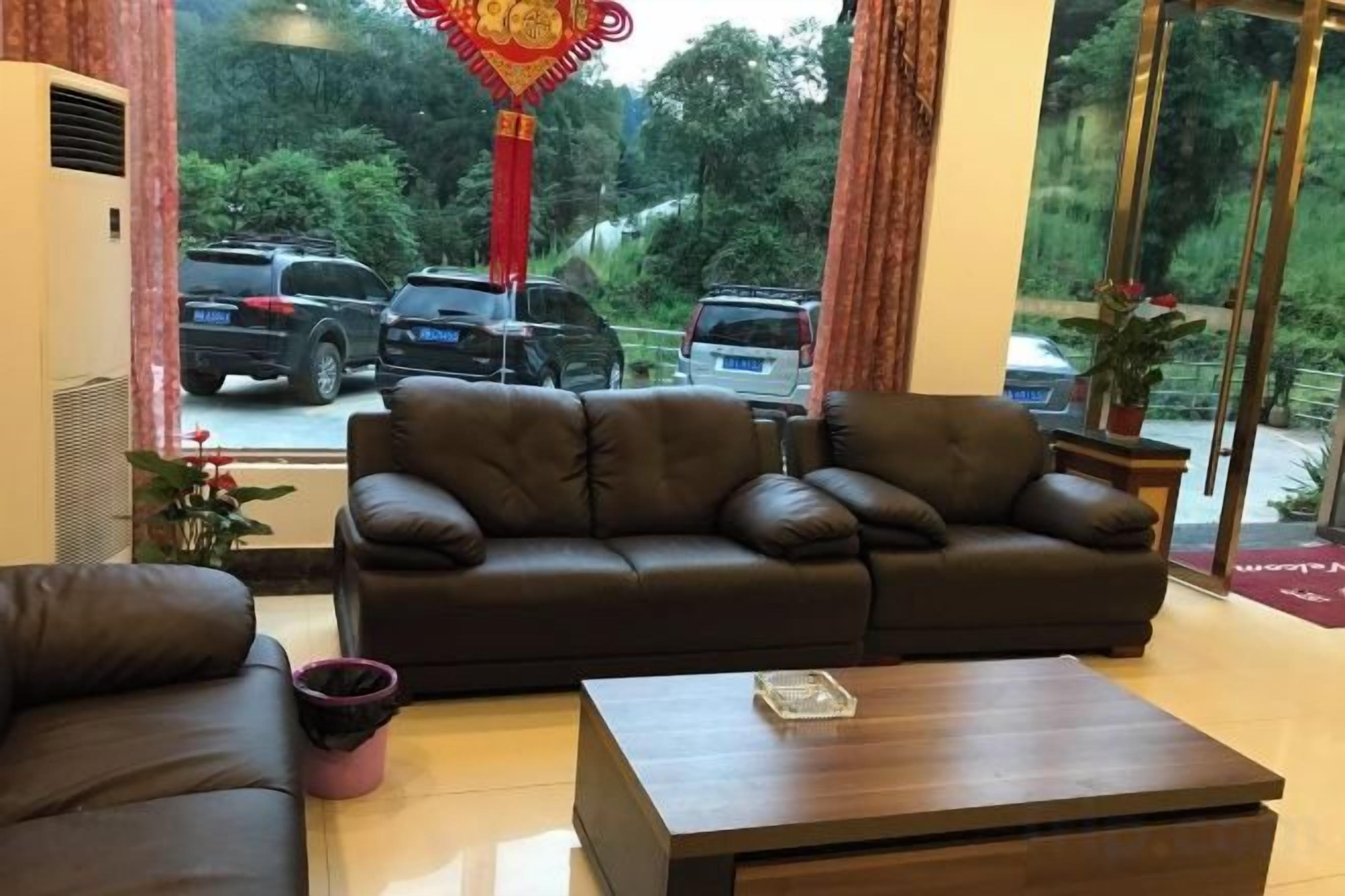 A hotel lobby with a leather sofa, a wooden coffee table, and a view of parked cars and greenery outside.