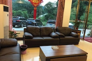 A hotel lobby with a leather sofa, a wooden coffee table, and a view of parked cars and greenery outside. - Mount Emei Feng Lin Yue Hotel (Emeishan City)