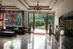 A modern hotel lobby with a sofa set, a television, and a view of a garden through the glass doors. - Mount Emei Feng Lin Yue Hotel (Emeishan City)