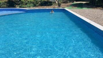 Una piscina rectangular con agua cristalina azul, rodeada por un borde de guijarros y un borde de baldosas.