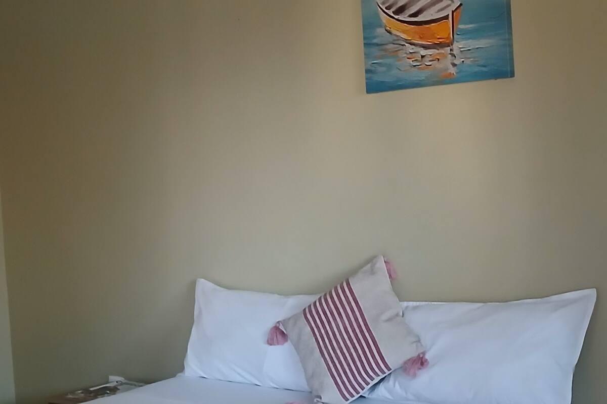 A neatly made bed with white linens, a striped pillow, and rolled towels on the side.
