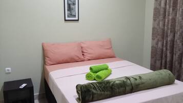 Un dormitorio con cama, almohadas, una mesita de noche, un cuadro en la pared y una cortina.