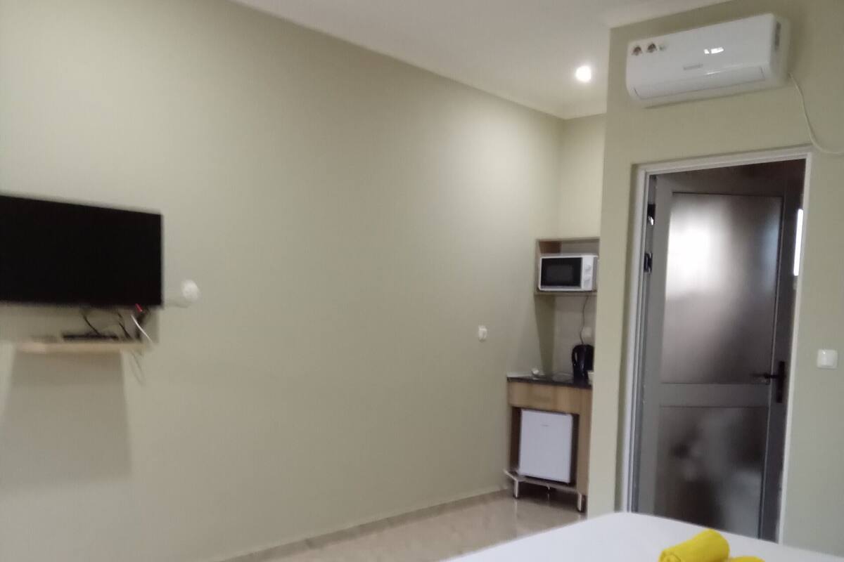 A hotel room with a bed, a flat-screen TV mounted on the wall, a microwave, and a door.