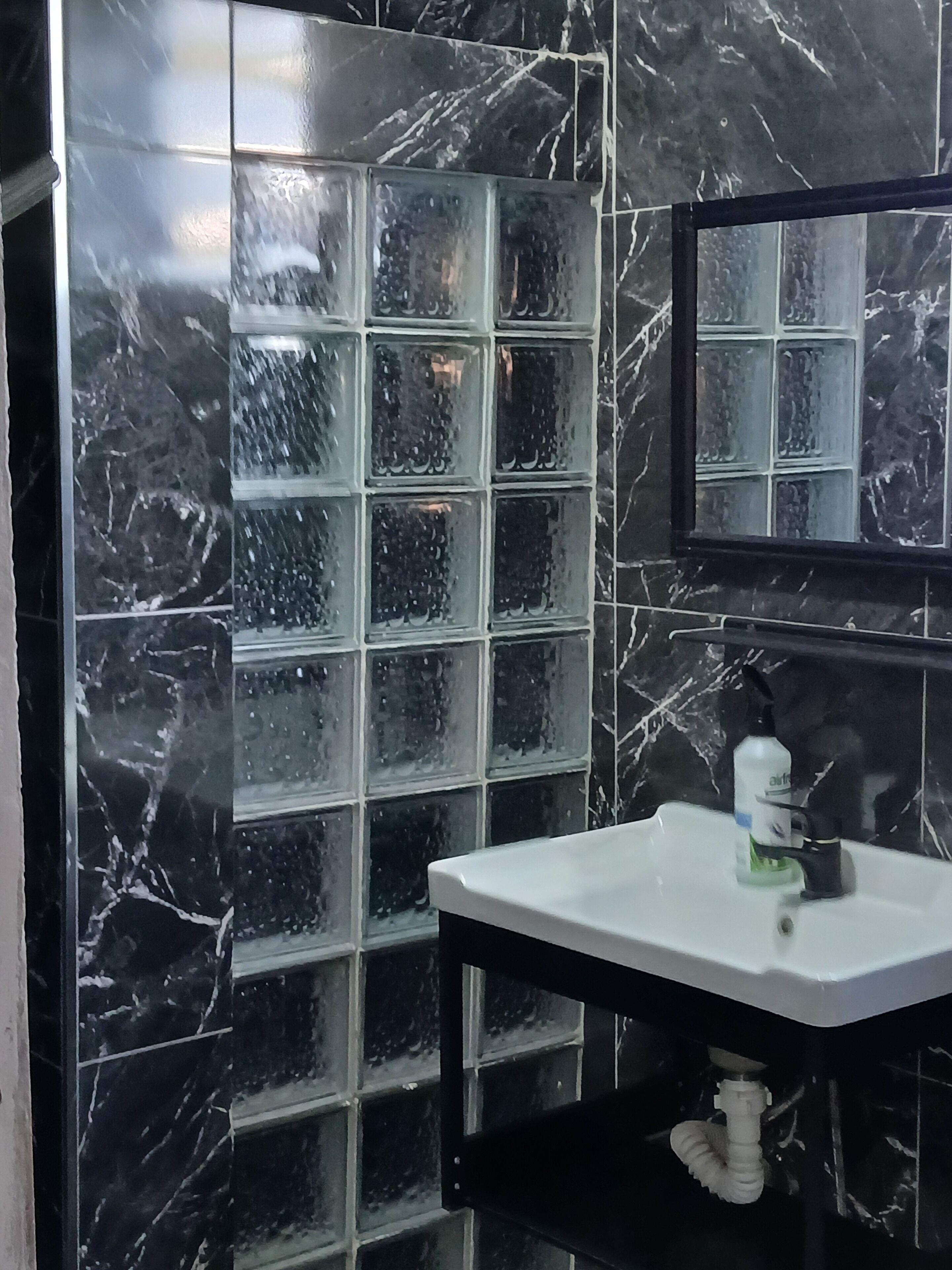 A bathroom with a black marble wall, a glass block partition, and a white sink with a faucet.