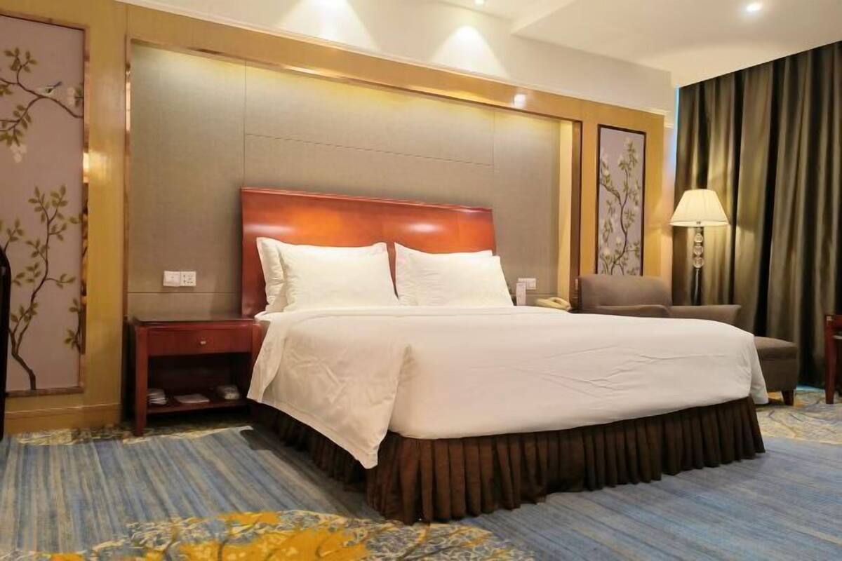 A hotel room with a large bed, a nightstand, a chair, a lamp, and a decorative wall panel.