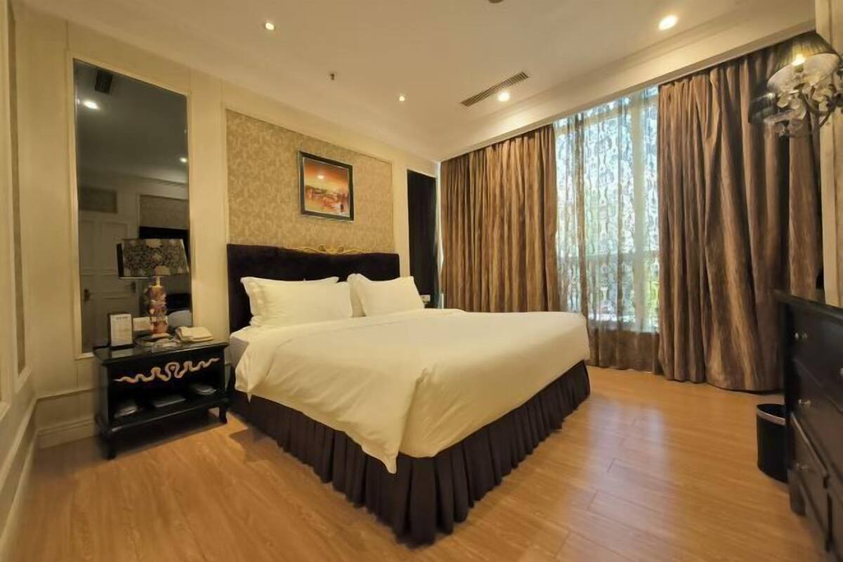 A bedroom with a large bed, a nightstand, a dresser, and a window with curtains.