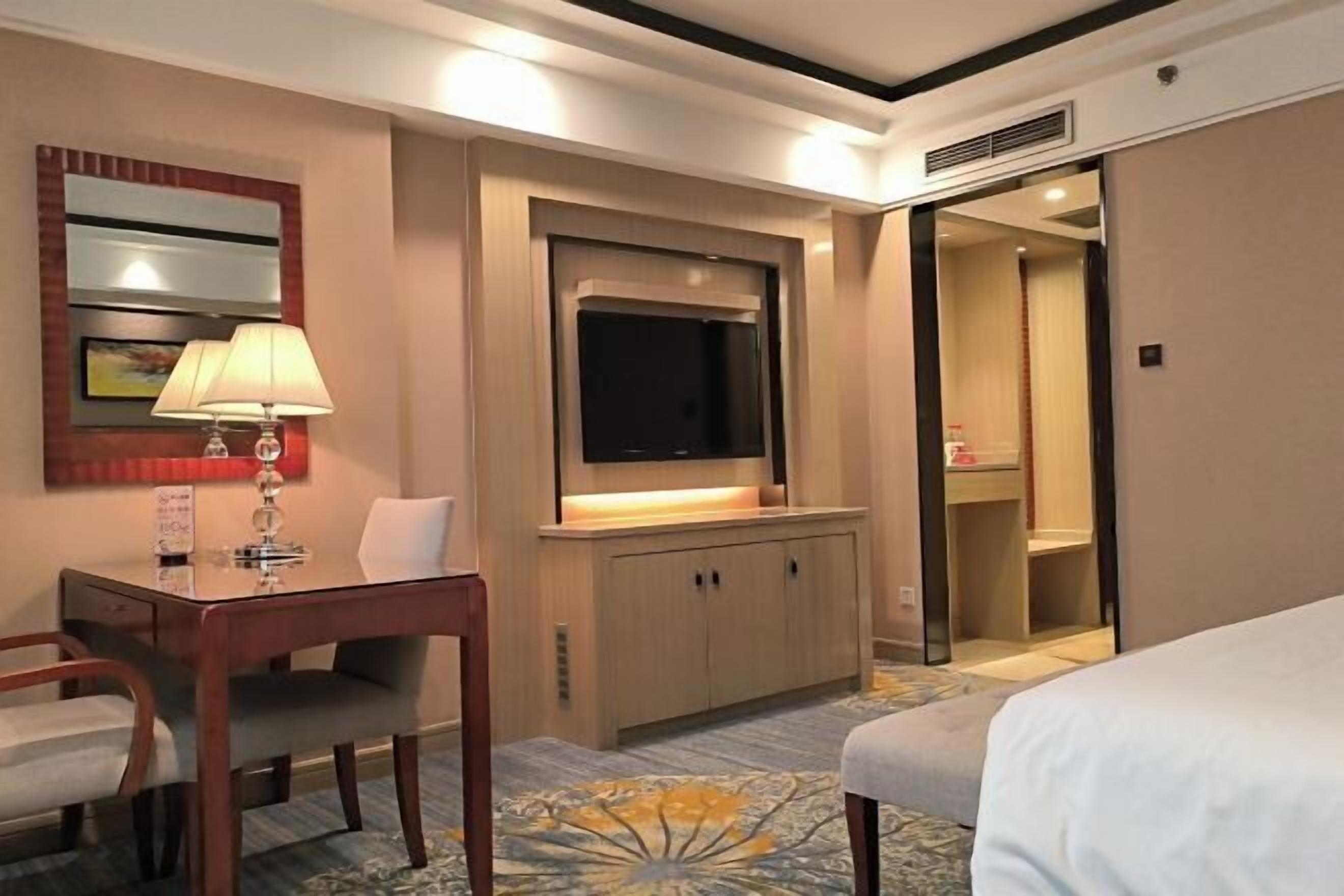 Een hotelkamer met een bed, een bureau met lamp, een televisie en een kledingkast.