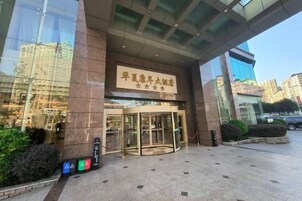 Entrada de un hotel con puerta giratoria, un letrero con caracteres chinos y el reflejo de un edificio en la fachada de vidrio.