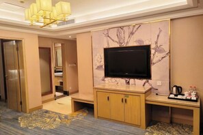 A hotel room with a flat-screen TV mounted on a wall with a floral design, a wooden cabinet with a coffee maker, and a patterned rug. - Huaxia Conifer Hotel (Dazhou)