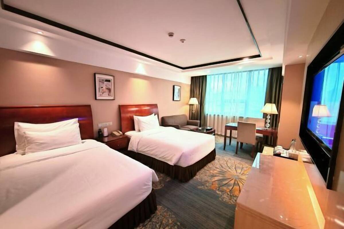 A hotel room with two beds, a desk, a TV, and a window with curtains.