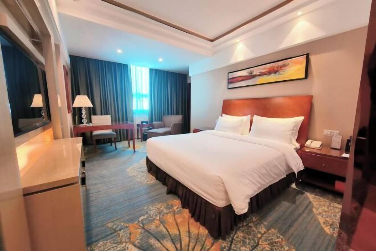 A hotel room with a large bed, a desk with a chair, a TV, and a window with curtains.
