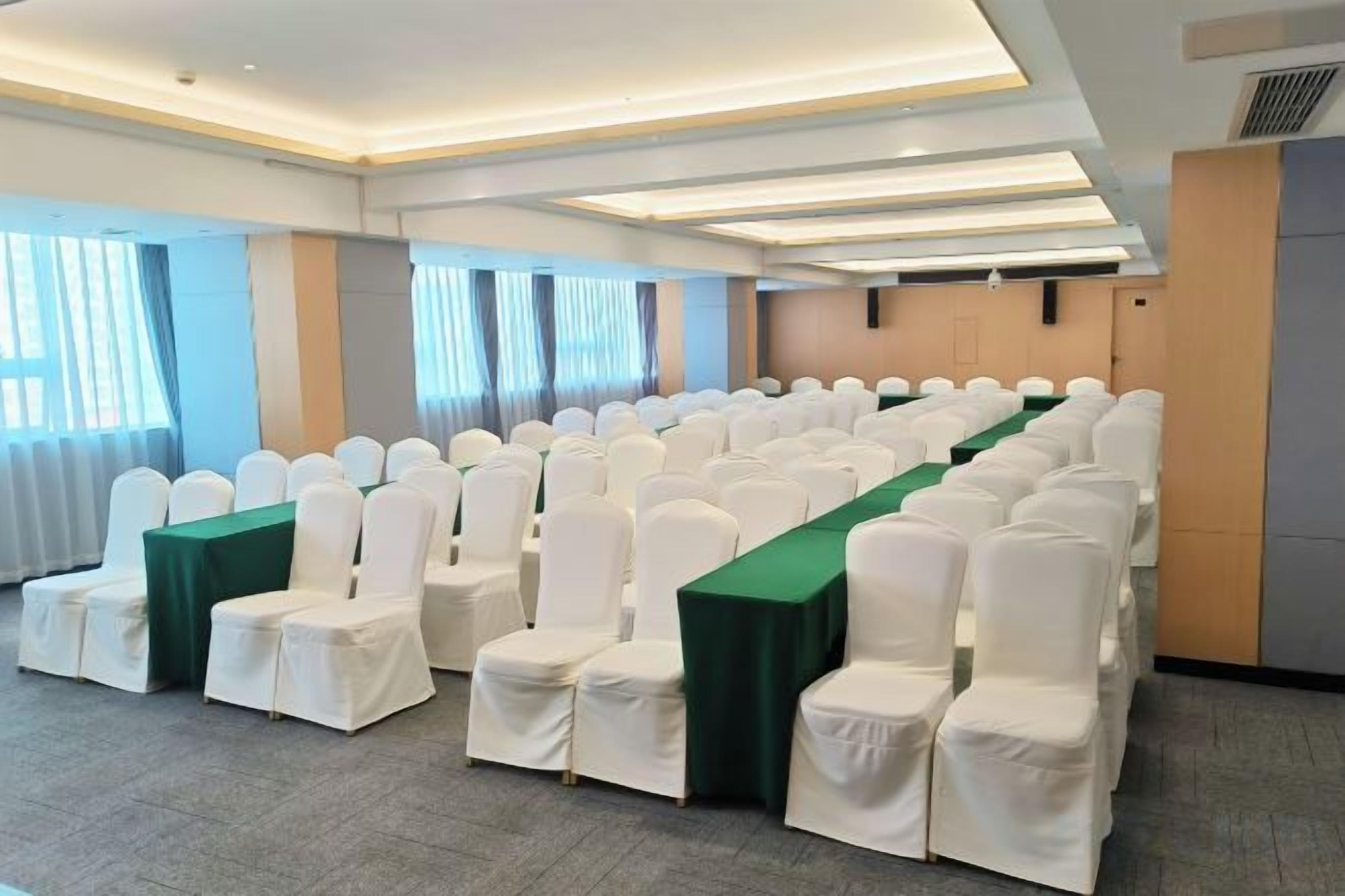 A conference room with rows of white chairs, a long table, and a neutral color scheme.