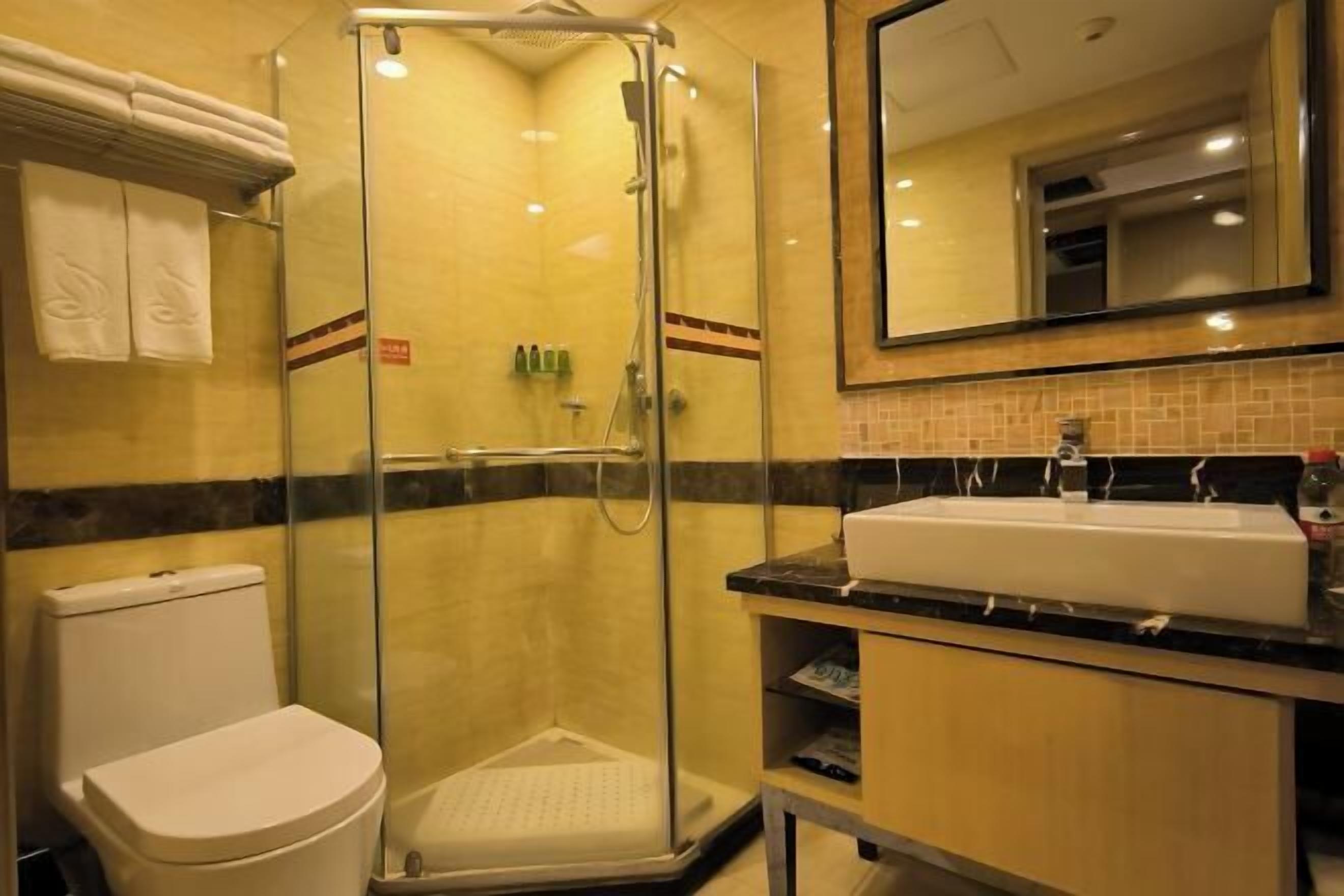A bathroom with a glass-enclosed shower, a white toilet, a sink with a mirror above it, and a tiled wall.