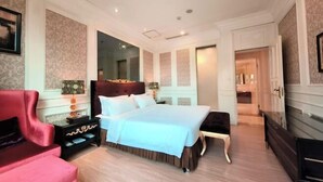 Un dormitorio amplio con una cama grande, un sillón rojo, una mesita de noche y un aparador.